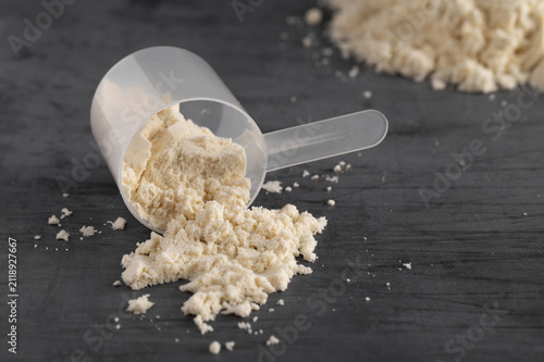 Measuring scoop with protein powder spilled on a dark background
