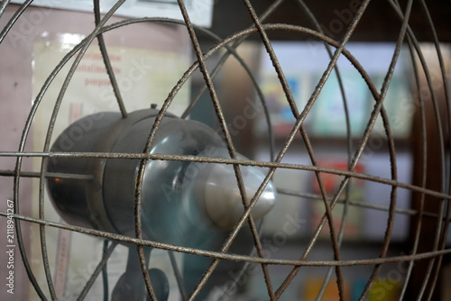 Close-Up Of Vintage Rusty Metal Fan Cage With Blurred Blades And Indoor Background