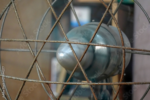 Close-Up Of Vintage Rusty Metal Fan Cage With Blurred Blades And Indoor Background
