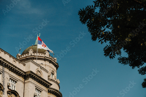 Quadro su tela Serbian national flag flying above a historic government building in Belgrade, Serbia