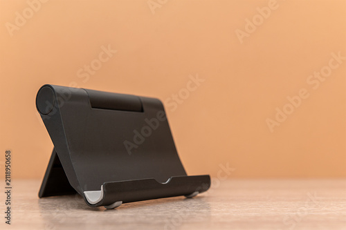 Black mobile phone stand on a beige background. Space for text.