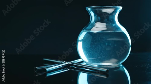 Blue rim light shapes a clear water carafe beside scattered reusable steel straws on a mirrored black surface, creating a moody sustainable drinkware still life with crisp reflections and copy space