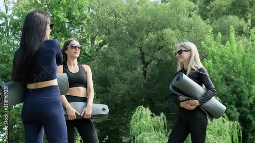 Women in stylish outfits comes together at fitness park, each carrying yoga mats, ready to embrace the tranquility and energy of shared workout experience. Ready for energetic workout