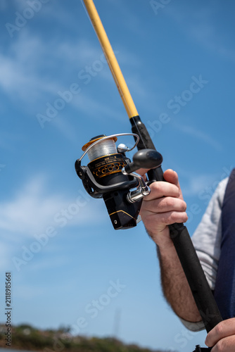 Fotografía Low angle view of fisherman holding fishing rod with spinning reel against blue