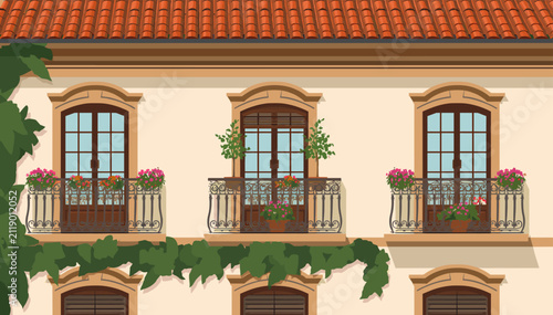 Photography Close-up view of a charming building facade with three balconies adorned with pink flowers, green plants, and climbing ivy under a terracotta tiled roof