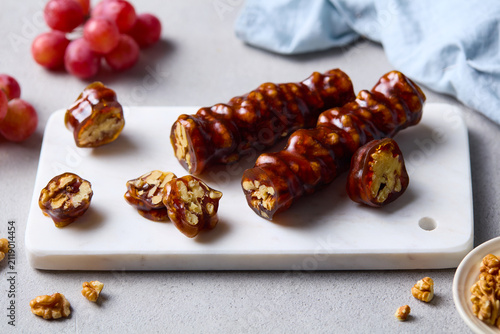 Traditional Georgian churchkhela sweet with red grapes and walnuts on marble board. Grey background. Close up.