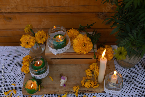 Close view of marigold altar arrangement with bright orange flowers, lit green candles inside mason jars wrapped with lace, wooden crate display, crocheted cloth, and tall warm ambient decor