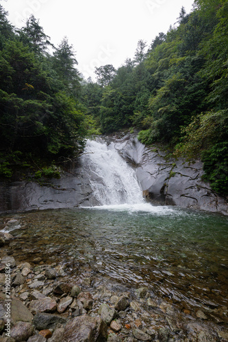 Serene waterfall cascading over smooth granite rocks into a clear emerald pool surrounded by lush green forest in Japan
