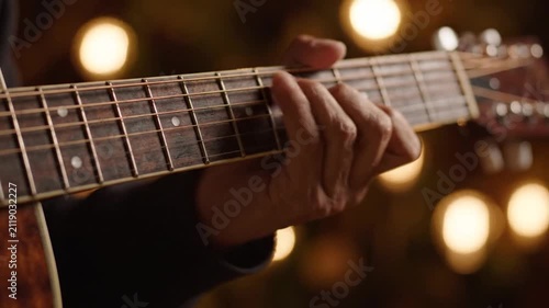 Close-up on a hand playing acoustic guitar with bokeh lights background