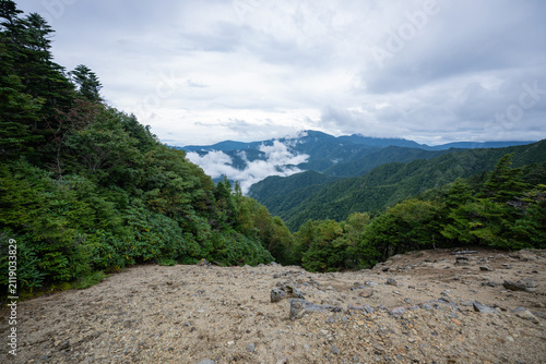 Panoramic mountain valley view from rocky outcrop with lush green forest and low clouds drifting through Japanese Alps