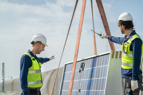 Two construction workers setting up solar panels at a clean energy location with bright blue skies overhead