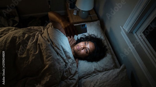 Young Woman Lying in Bed at Night Using Smartphone with Blue Light Illuminating Her Face, Symbolizing Digital Addiction and Insomnia