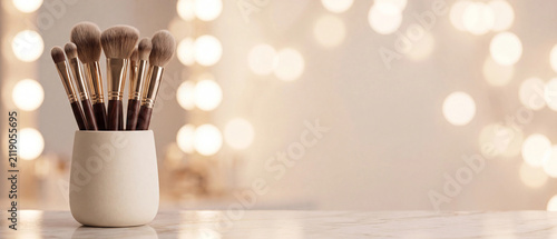 Makeup brushes in a holder on a marble table with blurred vanity lights in the background