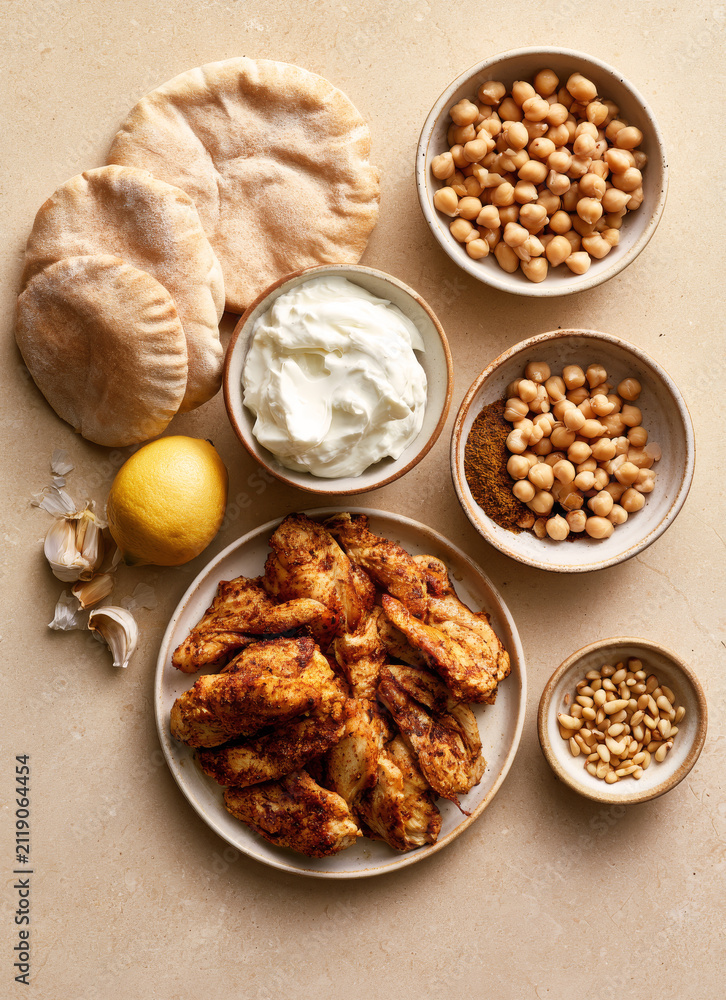 Fototapeta premium Ingredients for Mediterranean chicken shawarma bowl with pita bread, chickpeas, yogurt sauce, pine nuts, and lemon, top view.