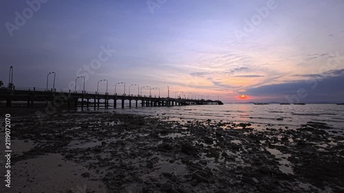 Long concrete pier over rocky tidal flats at tropical sunset