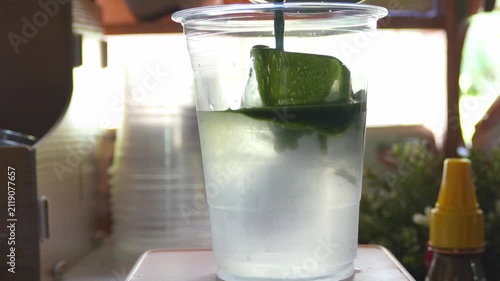 4K Pouring concentrated green tea matcha over coconut water with ice cubes in plastic cup at cozy cafe counter, Concept for matcha coconut iced tea barista craft and summer drink.