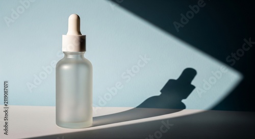 Empty frosted glass dropper bottle with a white cap, isolated on a light blue background with sharp geometric shadows for skincare
