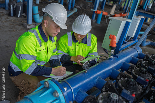 Technicians and engineers inspect a pressure gauge and industrial water pipeline system. Concept of engineering, water management, technical inspection, utilities, and industrial operations.