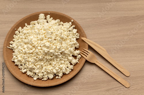 White crumbly cottage cheese on a craft plate against a wooden background. Space for text.