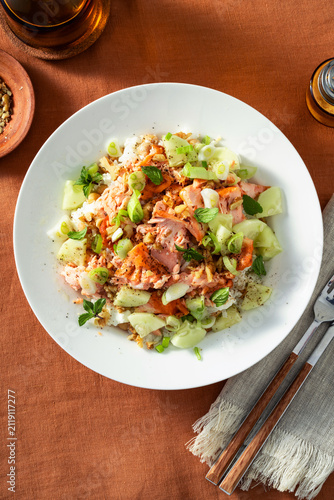 Close up of baked salmon salad with cucumbers, chickpeas, walnuts, feta and rice on a summer style dining table