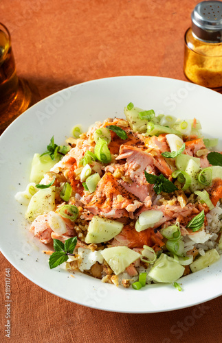 Close up of baked salmon salad with cucumbers, chickpeas, walnuts, feta and rice on a summer style dining table