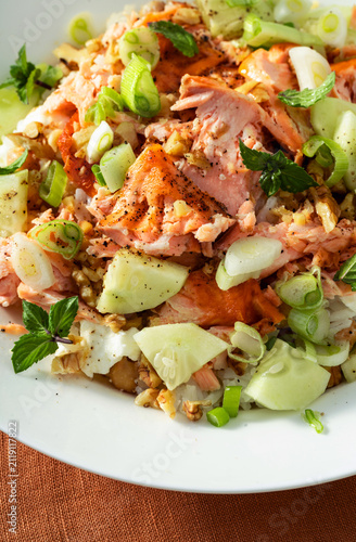 Close up of baked salmon salad with cucumbers, chickpeas, walnuts, feta and rice on a summer style dining table