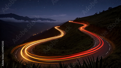 Long exposure shot of red car light trails on winding mountain road at night