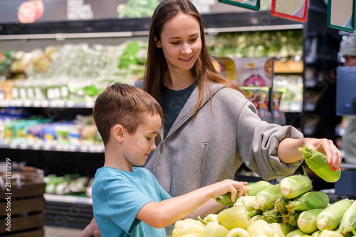 Mother and child shop for fresh corn in grocery aisle. Young boy looks up with curiosity, smiling at his mother.