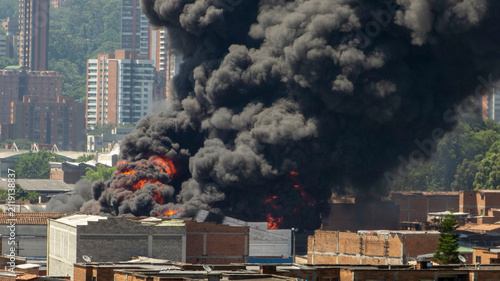 Large Urban Industrial Fire with Massive Black Smoke Plume Billowing Over a City Skyline and Residential Buildings
