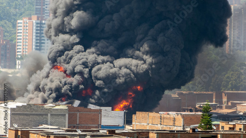 Large Urban Industrial Fire with Massive Black Smoke Plume Billowing Over a City Skyline and Residential Buildings