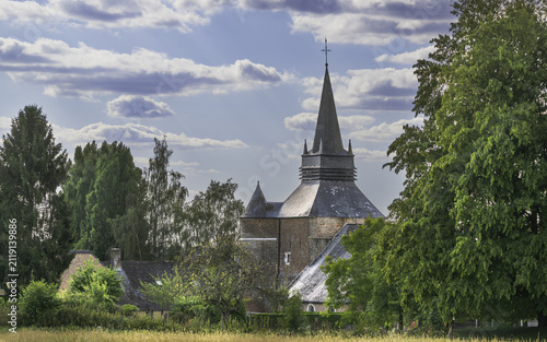 Saint-Medard fortified church with its tall slate spire rising above trees and village houses in Parfondeval, Aisne.