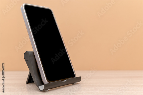 Black mobile phone stand on a beige background with a mobile phone. Space for text.