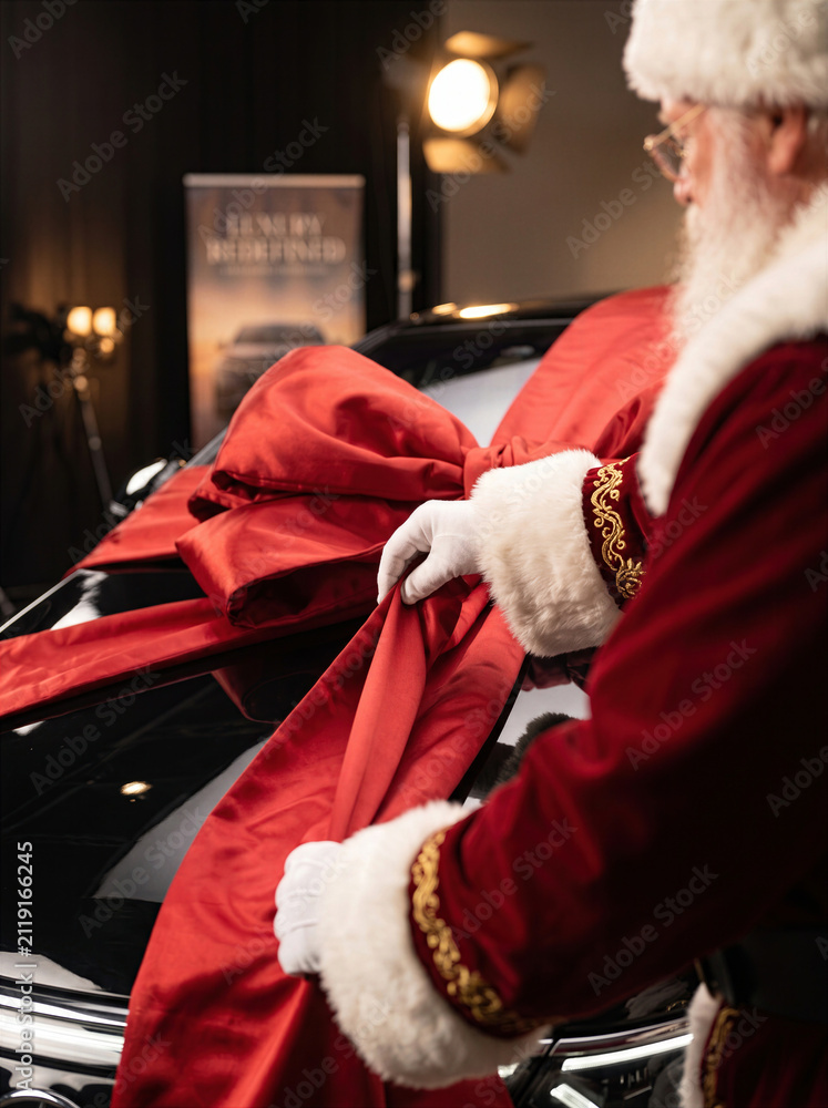 Obraz premium Santa Claus putting a large red bow on a luxury black car as a Christmas surprise gift in a professional showroom
