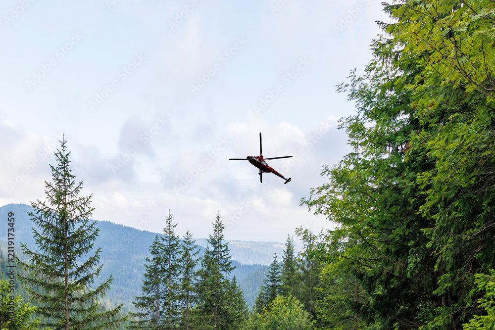 Fototapeta premium Rescue Helicopter Flying Over Green Mountain Forest Landscape