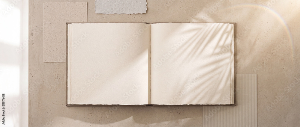 Fototapeta premium Open book mockup with blank pages lying on a neutral beige plaster background with palm shadows, ideal for aesthetic branding, artwork presentation, or portfolio design