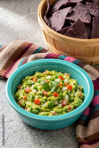 Fresh guacamole dip in teal bowl with purple tortilla chips in basket