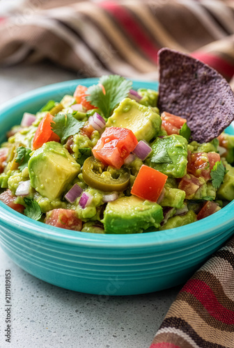 Close up of chunky guacamole dip with diced avocados tomatoes jalapeno and purple tortilla chip