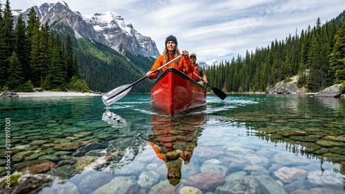 Canoeists paddle across a crystal clear mountain lake reflecting the majestic snow-capped peaks in the serene water.