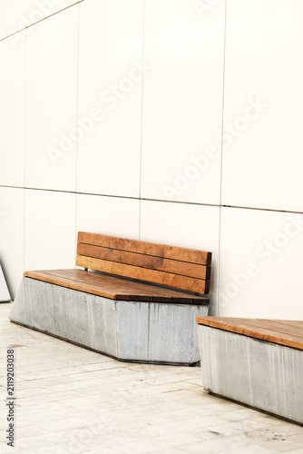 Modern urban wooden bench with solid concrete base against white clean wall facade. Street furniture in residential complex courtyard or business park.