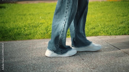 Side close-up of an anonymous woman's feet walking on a street with grass in the background, showing movement, nature, and outdoor lifestyle.
