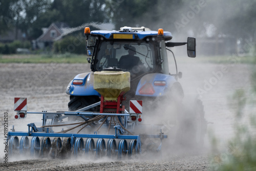 Rear view of  Blue Tractor Working on Dry Dusty Farmland