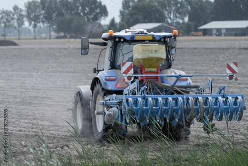 Rear view of  Blue Tractor Working on Dry Dusty Farmland