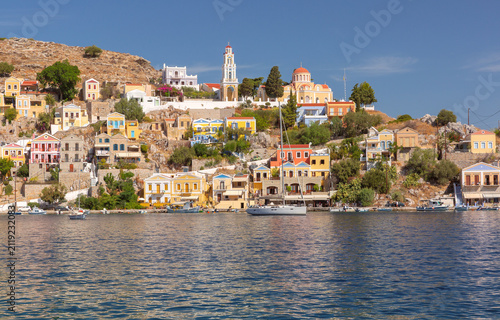 фотографія View of the waterfront with the historic clock tower and colorful hillside houses in Symi Harbor, Dodecanese, Greece
