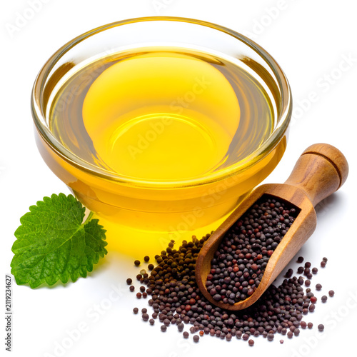 Glass bowl of oil with wooden scoop of mustard seed on white background