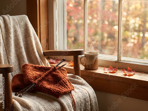 Cozy autumn scene with half-finished knitted scarf on needles by window with tea
