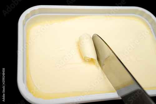 Фотография Butter is being spread using a knife from a container in a kitchen setting