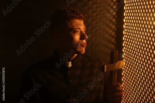 Bild auf Leinwand Priest with cross during confession near wooden window in booth