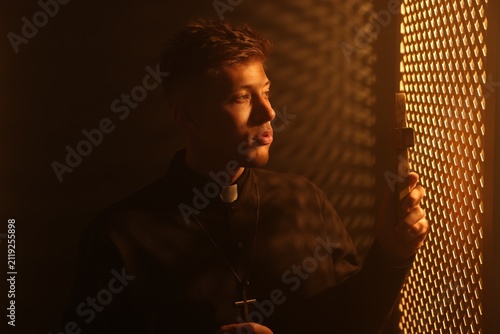 Bild auf Leinwand Priest with cross during confession near wooden window in booth