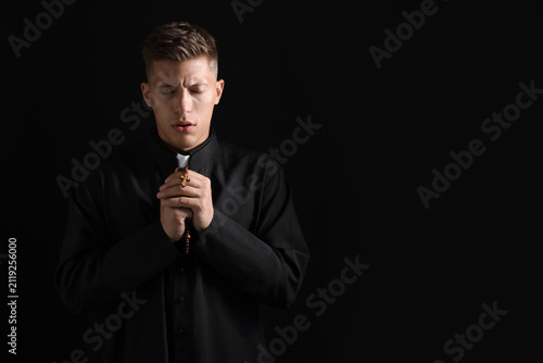 Konstfotografi Priest with rosary praying on black background. Space for text