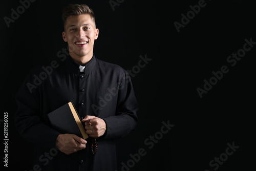 Foto Portrait of smiling priest with Holy Bible and rosary on black background